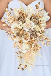 If you have chosen gold as your accent color, then look no further. This striking cascading brides’ bouquet is the perfect option for those who want to incorporate gold and champagne into their wedding. This bouquet is made using an array of gorgeous champagne roses accented with sparkly gold glitter roses and an abundance of mixed grasses and pampas. Gold accent foliage adds the perfect finishing touch to this unique arrangement that is absolutely stunning. Like all of our bouquets, this brides