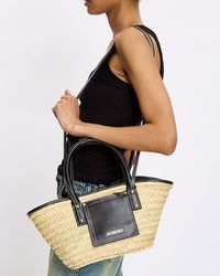 Jacquemus Le Petit Panier Soli in black features a handwoven basket bag with smooth leather details, long cross-body strap, top handle with pipe edges, front flap pocket and gold metal logo and studs.