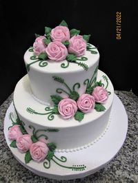 Two tier white buttercream cake with small white beaded borders and pink roses with green leaves