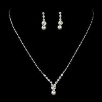 Enhance your wedding attire with this dainty and delicate pearl and rhinestone jewelry set. The slender silver necklace culminates in a charming pearl drop, while the matching earrings add a subtle sparkle. This set is the perfect blend of simplicity and elegance for any bride seeking a refined look on her special day. The necklace has a lobster claw clasp. Earrings has post back closure for pierced ears. Material: Crystals, Rhinestones, White Pearl, Shiny Metal Casting, Rhodium Plated Dimension