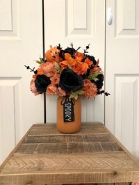 "This listing is for ONE arrangement.  This artificial arrangement is really pretty...it would be the perfect addition to your Halloween decor! The base of this piece is an orange mason jar. The jar has a \"Spooky\" tag tied around the mouth with black twine. I secured floral foam inside of the jar and then added each flower, piece of greenery and embellishment individually until complete. You are getting a HANDMADE floral arrangement! :-)  This beautifully spooky piece features a variety of flowers including black roses, orange hydrangea and more! It is approximately 12 inches tall by 10 inches wide. Please view the photos for measurement references.  This artificial arrangement would look wonderful displayed on your Halloween party buffet table. You could also take it to the office or gi