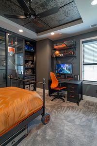 Desk and chair, industrial ceiling lights, black window frames, gray walls, orange used as an accent color, bookshelves, a carpeted floor, sports themed decorations, a basketball theme, sci-fi elements.