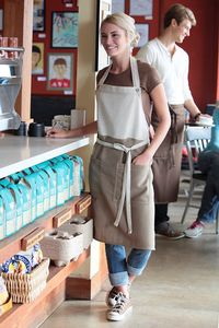 The Soho bib apron. Natural/camel colour. The perfect combination of edgy fashion and forward-thinking functionality. Featuring a contrast color block, buttoned neck strap, reinforced stress points and two patch pockets. Perfect for any kitchen, cafe or restaurant.