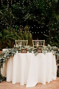 Mesa dos noivos decorada em greenery, com plaquinhas de madeira e decoração de luzinhas. #casamento #wedding #decoracaodecasamento #weddingdecor #stringlightswedding #bohowedding