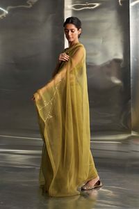 Embrace timeless elegance with this stunning berry green sari, crafted from pure organza fabric. Adorned with intricate golden nakshi hand embroidery inspired by graceful leaf motifs, it exudes richness and vibrancy. The ensemble is completed with a deep-neck, sleeveless padded chanderi blouse, adding a touch of glamour to this sophisticated outfit.