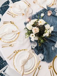 The winter wedding table details of your dreams. This table has the perfect white table cloth, simple white plates, with a gold rimmed charger plate, gold utensils, white napkins, white flowers, and navy blue table runner. The perfect amount of lively colors with plain colors to tie everything together. Mat Schramm Photography