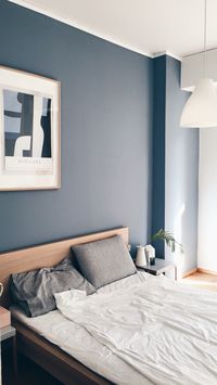 Minimalist bedroom with blue grey wall and moralis painting hanging on the wall.