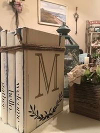 Farmhouse style Painted book stack paired with A size Welcome Transfer and Monogram M Transfer from Chalk Couture With Black and Gold Chalk Paste. #monogram #bookstack #farmhouse #chalkcouture #welcome #homedecor #askmehow #comejoinme #chippy #acrylicpaints #bookstagram ChalkCouture.com/ShesCrafty