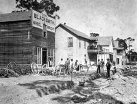 Early street scene on North Miami Avenue - Miami, Florida: Shows the blacksmith shop of C. Cone, one of Miami's first blacksmiths. Next to it is the groceries and grain store of T. N. Gautier. Upstairs, Mrs. Gautier ran one of Miami's early boarding houses. (1896)