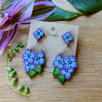 These blue hydrangea flowers are a stunning pair of chandelier earrings with cascading blossoms and sparkling silver chain for an elegant statement! These original earrings feature two pieces of hand painted and etched cherry wood with a palette of blues, lavender, and green. Extremely lightweight and unique, these detailed earrings will add a vibrant botanical touch to your collection and make a great gift for a plant lover. Get ready for compliments! These earrings feature hypoallergenic silve