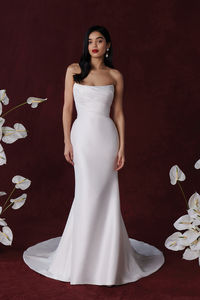 This elegant strapless fit and flare wedding dress features unique draping across the bodice and flows effortlessly with the mikado skirt. The fabric covered buttons trail down the end of the train.