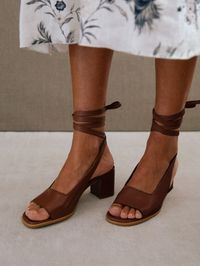 Sandalias peep toe marrones de piel con tacón cuadrado ¿Alguna vez te has preguntado qué usan las francesas en verano? Te presentamos a Lille, las elegantes sandalias peep-toe à la ALOHAS. Confeccionadas en cuero marrón flexible, están diseñadas con la silueta del clásico de zapato de salón, pero tienen cómodos tacones cuadrados para el día. Los largos lazos se envuelven con elegancia alrededor del tobillo, y voilà, son un par perfecto para aportar un toque sofisticado a cualquier look.