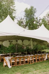 At this tented wedding reception in Colorado guests sat at long wedding tables with folded wood chairs and organic wedding flowers. The tented wedding reception tent was filled with white paper lanterns and bistro lights. Save this photo to your wedding planning board if you are looking for tented wedding reception ideas.| Amber Vickery Photography