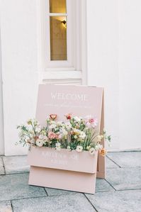 A pale pink welcome sign with a built-in flower box in shades of white, pink and coral handcrafted by the bride and groom for their artful, elegant estate garden wedding.