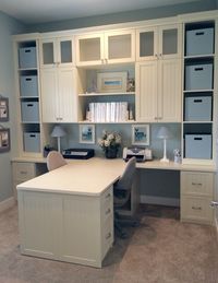 The office has a shared desk and lots of storage with cloth totes on shelves as well as drawers with hanging files inside.