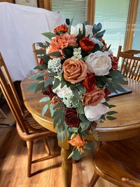 This is a fall cascade of terracotta, cream, burnt orange, and peach with sage colored greenery. Inspired by The color collection Terracotta Sunset this bouquet will be beautiful for your fall wedding.  It is made on a traditional bouquet holder that can be wrapped in ribbon or burlap to conceal.  It is 22 inches long. Also pictured are large round bridesmaids bouquets. I can created pieces for your entire wedding party if you choose.