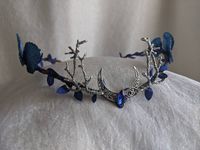 An ethereal woodland tiara featuring sapphire blue leaves (including large blue leaves) surrounding the piece and a moon charm with crystal in the center and two branches at its side. Perfect for special occasions or to add a bit of magic to your every day! The secondary color refers to the metal (silver pictured).