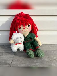 Red headed fabric doll holding her precious pup. The pup is wearing a Santa hat!