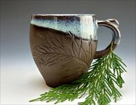 The new Cypress Collection uses real Cypress fronds embossed into the wet clay for a luscious tactile texture. Each piece is a one-of-a-kind and I photograph them individually. Nature-lovers, city-dwellers, and tree-huggers alike love them. Even with eyes closed, you will feel at peace with nature. The handle includes a thumb grip, is balanced, and makes them easily stackable. The insides are fully glazed, while the outsides are diagonally rim glazed, showing the luxuriously natural near-black c