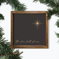 The star still shines.  His light still shines today. Accent your Christmas decor with this stunning printed sign with a gold foil star, soft black background and shiny gold splashes resting behind the star. Artwork is printed on 100% canvas. The frame is made of pine wood and finished with a walnut stain to enhance the natural grain. The box framed wall decor will make a wonderful gift for someone special this holiday season for a wall or table. Choose from a 6x6, 8x8, or 10x10 inches walnut st