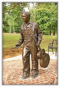 Elvis Presley statue | Tupelo, Mississippi birthplace ~ created by sculptor Michiel Van der Sommen - cost $50,000. "We chose 13 because that was the age his family left and went to Memphis," The goal was to depict Elvis in his "innocence and humbleness."  It depicts a boy who doesn't quite resemble the face the whole world knows. The 13-year-old dressed in overalls carries a guitar at his left side with his right hand reaching forward.