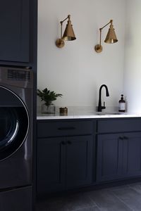 Monochormatic laundry room. Dark blue cabinetry. Brass conical ilghts.