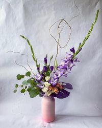 A unique and trendy flower arrangement in a pink vase, featuring gladiolus, silver dollar eucalyptus, lisianthus, spray roses, and painted monstera.