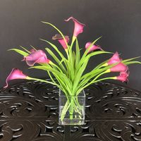 This gorgeous silk flower arrangement consists of 9 silk calla lilies decorated with flax leaves in a cube glass vase for the perfect modern centerpiece. Handcrafted for lasting beauty, this artful silk flower arrangement uses acrylic water and is styled in a 5" cubed vase. #moderncenterpice #modernflowerarrangement #callalilies #silkflowerarrangement #homedecor #luxuryhomedecor