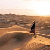 An aesthetic photograph of a model standing in the dunes of a desert.