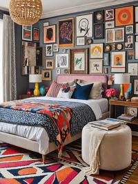 Discover the charm of eclectic interior design with this vibrant bedroom decor. The space features a gallery wall with an array of framed artworks, providing an artistic backdrop. The room combines a variety of textures and patterns, including a woven ceiling light fixture, a multi-colored patterned quilt, and a bold area rug with geometric designs. Accentuated by a neutral upholstered bed and a cozy round ottoman, the bedroom strikes a balance between comfort and style. The image showcases ...