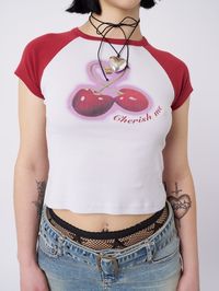 Craving a fun and vibrant addition to your wardrobe? Our Cherry Pop! Raglan Baby Tee has you covered. Combining our favorite fruit with a baby tee style, this baseball tee in red and white offers a playful and eye-catching look. Bold Design: Contrast raglan sleeves "Cherish me" front graphic print Comfort & Fit: Cropped length Short sleeves Crew neck 100% cotton material for a soft and breathable feel Model Info: Tani wears size M and is 176 cm | 5'9" tall Patrícia wears size S and is 165 cm | 5