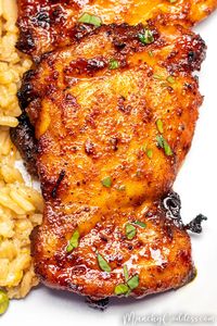 Air fryer boneless skinless chicken thigh topped with chopped parsley next to a bed of fried rice on a light gray plate.