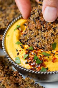 dipping quinoa cumin crackers in carrot hummus