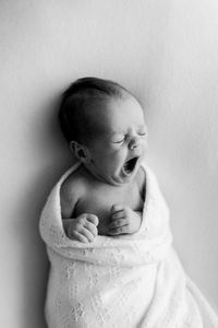 Black and white photo of a baby yawning, wrapped in a merino heirloom blanket during newborn session.