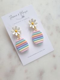 Whimsical Pastel Stripe Easter Egg Earrings with Golden Daisy Stud * Rainbow striped Easter Egg with Daisy charm stud * Gold plated stainless steel * 4.5cm length * Made from Polymer clay, so lightweight and durable * Add a pop of colour to your outfit Description: Celebrate the joy of Easter with these whimsical Pastel Stripe Easter Egg Earrings! Each earring features a charming polymer clay Easter egg adorned with a golden daisy stud. These lightweight and comfortable earrings are perfect for