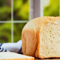 front shot of bread loaf on right side sliced to reveal the inside with a slice lying down on the bottom left side.