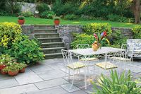 The rough stones in a retaining wall contrast nicely with the smooth bluestone on this sunken patio. Adding even more interest are the various sizes of pavers and the mix of colors, including shades of blue, gray, and purple. The patio's joints fit so tightly that the surface is smooth enough to roll out a charcoal kettle for barbecues.  Learn how to install a cut bluestone patio.  Similar to shown: PA Full Color Natural Cleft bluestone, $5.75 per square foot, thestonecenter.com