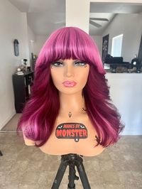 "*Made To Order Wig. Please allow 2 to 3 weeks for processing time* Custom colored pink wig with a dark magenta red halo. Shag cut with bangs and heavy face framing layers Lace free bang wig. Ready to wear glueless wig. Easy to pop on and off for a quick look. 180% Density. Cap Size - Average. 21.5\" / 22\" Circumference Combs inside cap and adjustable straps for a secure fit. Texture - Slight wave (3rd Picture is wig air dried with no product) 100% Indian Virgin Remy Human Hair Can be heat styled or colored. *Wig pictured is 16 inches* *All Manes By Monster wigs have been colored & styled with professional salon quality products* *Due to wigs being human hair, best results are achieved when hair has been heat styled or product is used. A light pomade or spray wax to tame any flyaway hairs