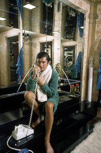 VP of Paramount Pictures Robert Evans in terry robe, sitting on edge of black marble tub talking on phone, in bathroom at home. Nov. 1968