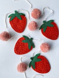 Add a little sweetness to your bedroom, kitchen, or nursery with this handmade felt strawberry garland! Use it for seasonal decoration or hang it up year round. Each garland has four two-dimensional strawberries measuring four inches in length, with five pink pompoms measuring approximately one and a half inches across, all strung on a five-foot length of white yarn. Each garland is hand-cut and hand-stitched, so details may vary slightly from product to product.