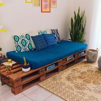 Sala de estar super aconchegante com um lindo sofá de pallets, muitas almofadas e uma composição de quadros na parede. Font