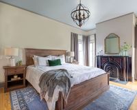 Historic bedroom. Crown molding. Natural light. Fireplace. Vintage blue rug. Classic style. Restful space.