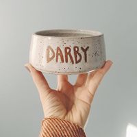 PLEASE NOTE: This listing is a pre-order for a custom bowl, which has a 3 week lead time. Handmade on the pottery wheel with speckled brownstone clay, this bowl is a sweet way to honor your furry best friend.   Glazed in clean white, this stoneware piece has your pet's name custom printed in capitol letters on the front using a wax resist technique. The sturdy and classically tapered shape assures it won't tip over. Custom dog bowls are available in three approximate sizes: 5" (holds about 1.5 c