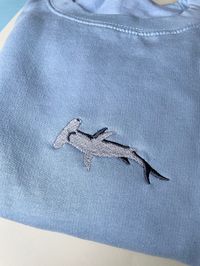 Hammerhead Shark Embroidered Jumper sweatshirt. Hammer head sharks are wonderful and magical creatures, their eyes on the side of their hammer head allow them to see 360-degrees. They can see above them and below them all the time. How amazing! Soft Cotton drop shoulder style with stylish fit. Designed and Embroidered in the UK. Unisex Fit. Vegan. We donate to animal charities.   JUMPER INFO Twin needle stitching Hammerhead shark. We use sustainable fabric and the jumper is fair trade certified.