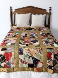 An antique crazy quilt blanket circa 1910. The patchwork quilt features multiple textiles with a gold satin border. There is an embroidered heart at the top. The backing is a soft gray cotton. - multi