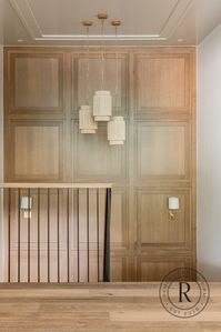 In this open space with soaring ceilings, we added this unique white oak millwork design, coffered ceilings, and these three pendants with varying lengths to fill that space, while still maintaining an open feeling in the stairwell.