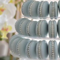 Get ready to wow your guests with our amazing Dusty Blue Pearl Macarons! These little beauties are made by hand with lots of love and careful attention to detail. The gorgeous design featuring edible pearls and a shimmery dusty blue shell is going to make jaws drop. Your friends and family won't be able to believe how insanely pretty these macarons look! But it's not just about the looks. They come with our signature flavor options, classic Vanilla Bean, and Blueberry Lemon. Each bite packs a ton of flavor into these lovely French treats.  Tower Display is not included. Whether you need a showstopping dessert for a party or just want to treat yourself, the Dusty Blue Pearl  Macarons are the way to go. Elegant yet fun, they're a dessert you'll never forget! We proudly produce our macarons i