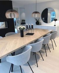 This beautifully designed dining room embodies a modern minimalist aesthetic with a touch of Scandinavian influence. The light wooden table, paired with soft gray upholstered chairs, creates a cozy yet elegant atmosphere. The black accents, including the sleek candle holder and pendant lights, add contrast and sophistication. The circular mirror on the wall further enhances the clean, open feel, while the monochromatic color palette maintains a calming, cohesive look. Perfect for those who appreciate simplicity and style in their living spaces.  modern dining room, minimalist design, Scandinavian style, light wood table, gray upholstered chairs, pendant lighting, black accents, circular mirror, sleek decor, contemporary dining room.