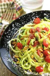 Close up view of a plate full of zucchini noodles with fresh tomatoes and pine nuts