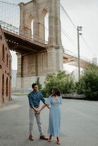 Couple walking in Dumbo Brooklyn with the Brooklyn Bridge in the background. New York City engagement session. Brooklyn Dumbo engagement session, Brooklyn wedding photographer, NYC wedding photographer. Anais Possamai Photography